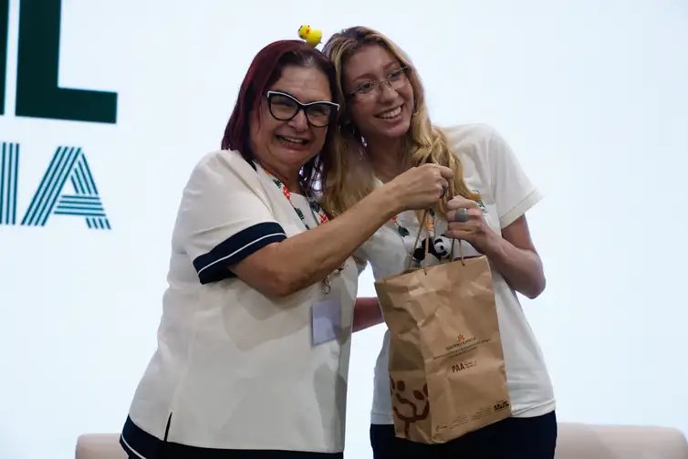 Tânia Rêgo/Agência Brasil Belém (PA), 17/11/2025 - A voluntaria Gabriella Araujo, recebe o kit durante ato de entrega simbólica dos kits da Agricultura Familiar (PAA) para os voluntários da COP30, no Pavilhão Brasil. Foto: Tânia Rêgo/Agência Brasil